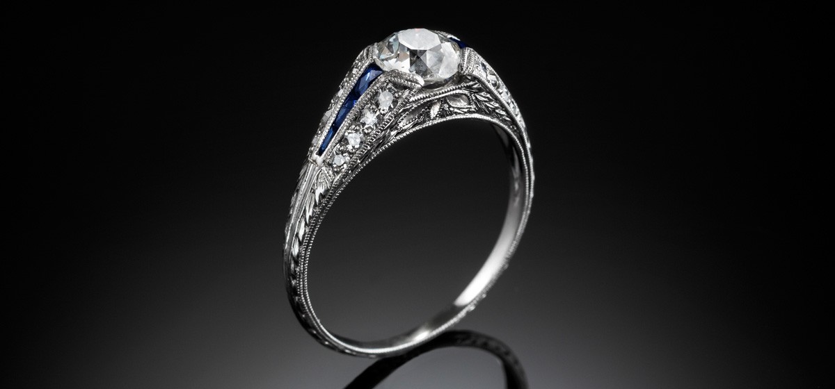 An Art Deco solitaire diamond ring with diamond and calibre cut sapphire shoulders