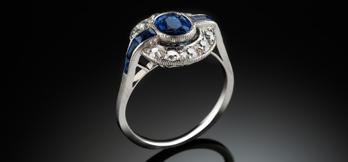 An Art Deco platinum, sapphire and diamond cluster ring with faceted sapphire shoulders