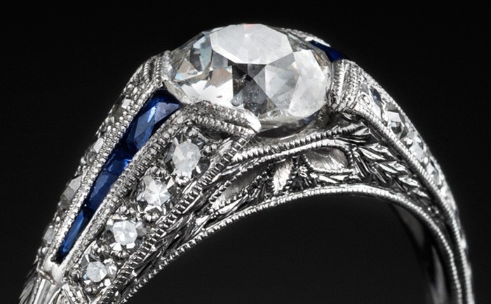 Detail of An Art Deco solitaire diamond ring with diamond and calibre cut sapphire shoulders