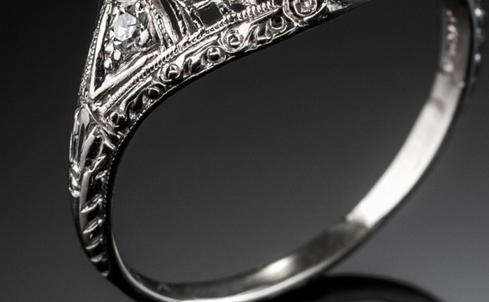 Detail of an Edwardian platinum and solitaire diamond ring in a diamond embellished domed mount